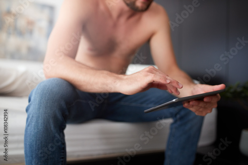 Young man sitting on the bed using digital tablet