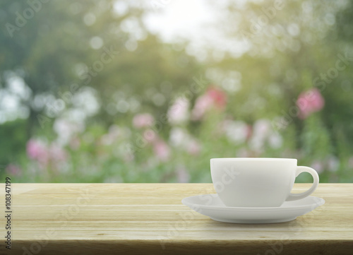 White cup on wooden table with blurred pink flower and tree, sof