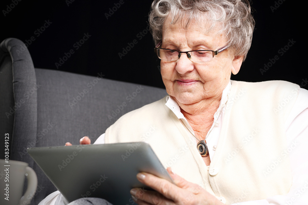 Starsza kobieta z tabletem.Starsza kobieta serfuje po internecie. - obrazy, fototapety, plakaty 