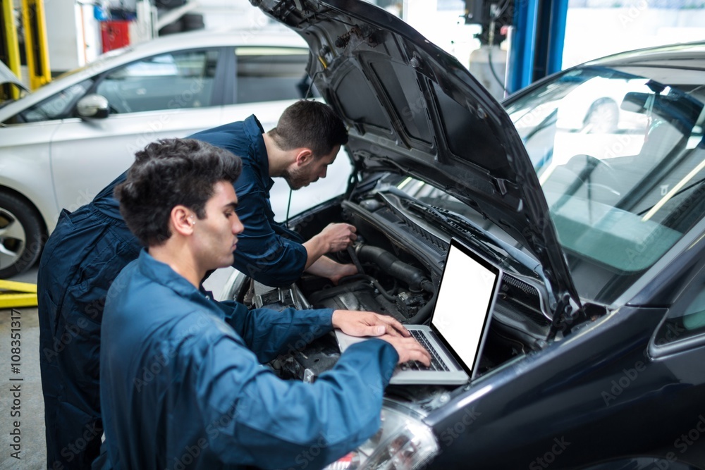 Mechanics examining car engine using laptop Mechanics examining car engine using laptop