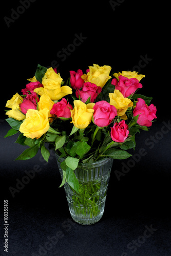Bouquets of fading yellow and pink roses in a glass vase