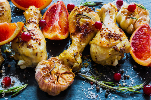 Roasted chicken legs, red oranges, cranberries, garlic and rosemary on the black background. Cooked with sauce from mustard, orange, honey and olive oil. photo