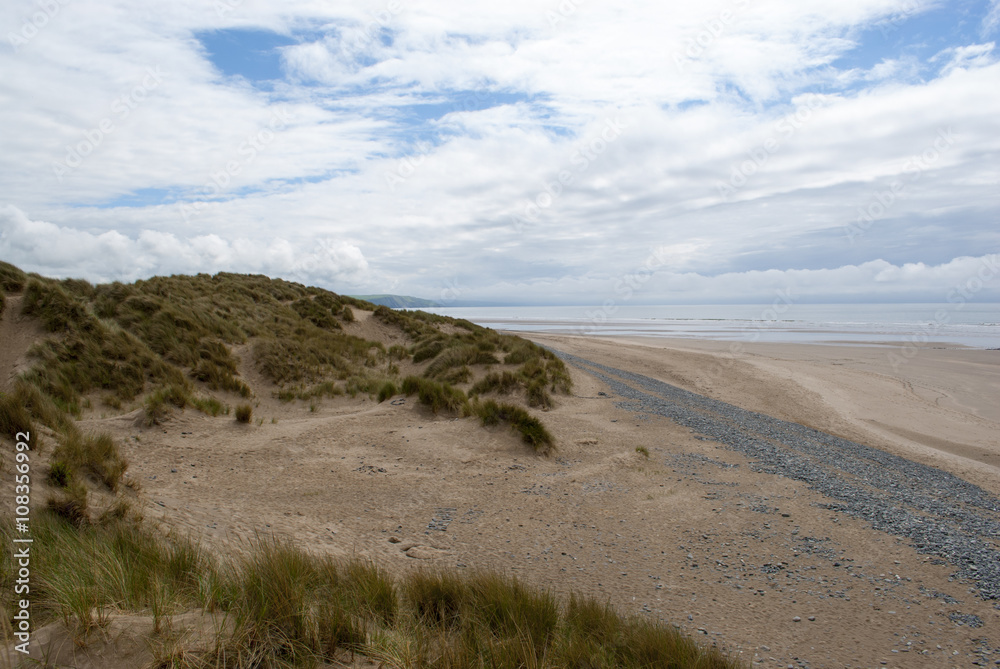 low down shot of beach with pebbles, grassy dunes and contrasting sky in Ynyslas, Wales, UK
