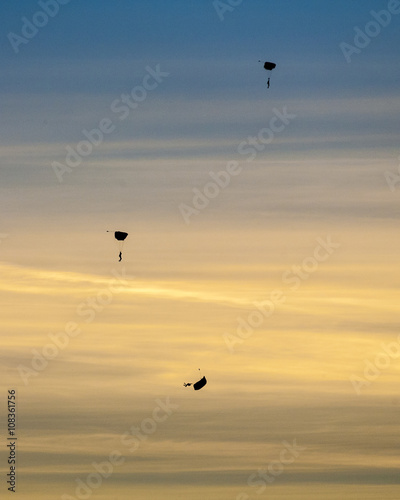Silhouette of three skydivers falling with parachute open against dramatice sunset and clouds