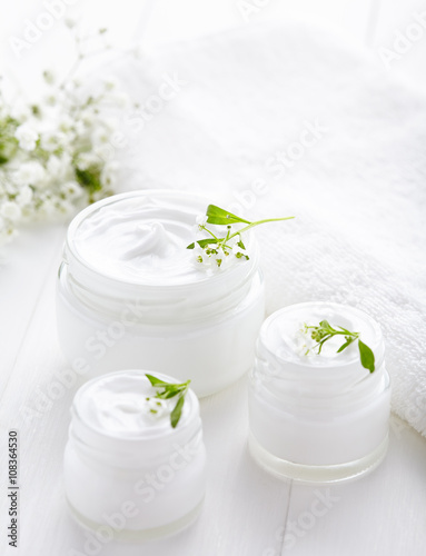 Dermatology herbal cosmetic cream with flowers hygienic skincare product in glass jar on white background