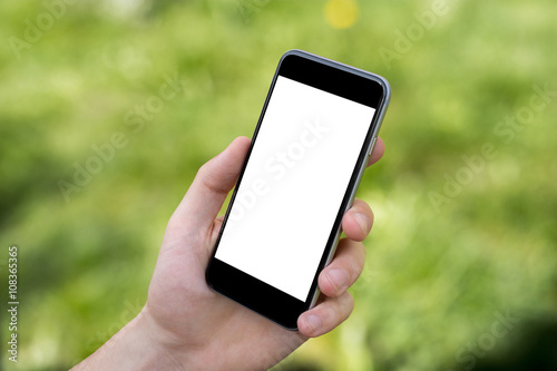 Hand holding black smartphone with blank screen against blurred grass background photo