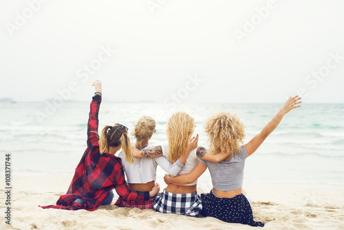 Group of young women sitting at the beach looking at the sea.