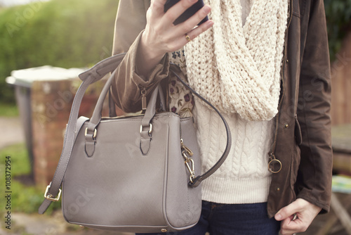 Woman Walking Outdoors Holding Handbag And Mobile Phone photo