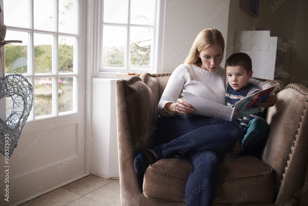 Mother reading story to her son while sitting on armchair at home Mother reading story to her son while sitting on armchair at home