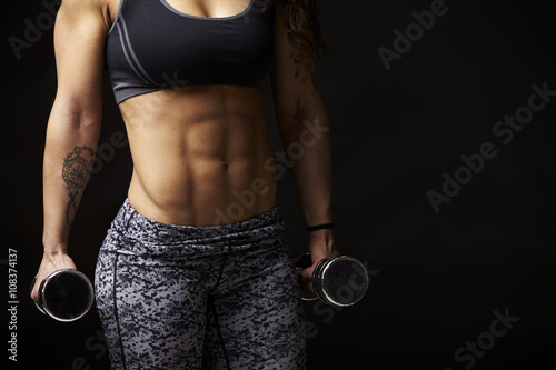 Mid-section crop of muscular young woman holding dumbbells