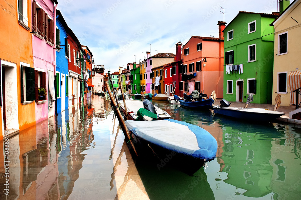 Colorful houses lined along the canal at Burano island, Venice, reflecting in wet street pavement