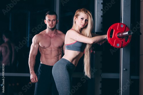 Young couple exercising in gym with weights  man seems to be the personal trainer