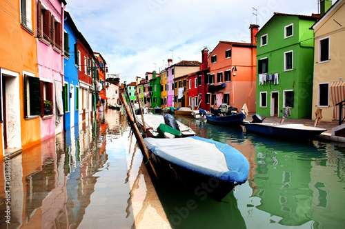 Colorful houses lined along the canal at Burano island, Venice, reflecting in wet street pavement © Olena Ilienko