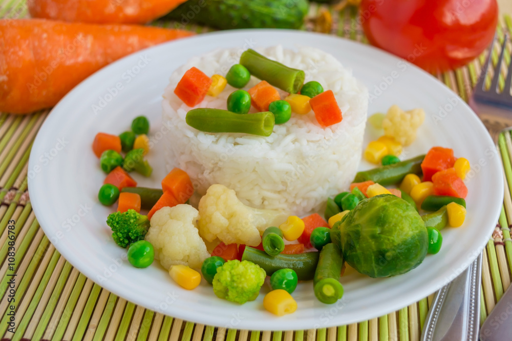 Rice with vegetables steamed on a white plate, laid out in a circle. Vegan. The top view. Rice with vegetables steamed on a white plate, laid out in a circle. Vegan. The top view.