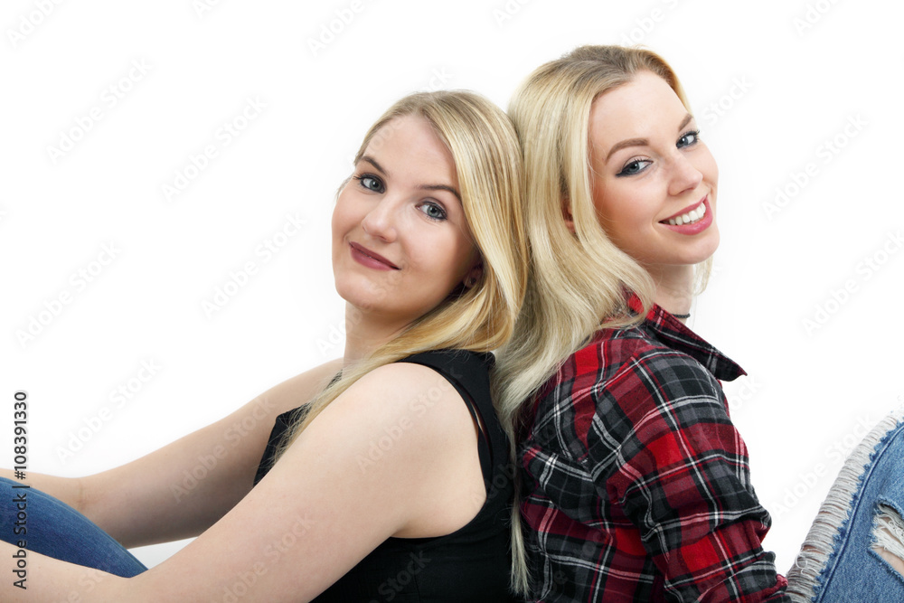 zwei junge Frauen sitzen Rücken an Rücken und lächeln 