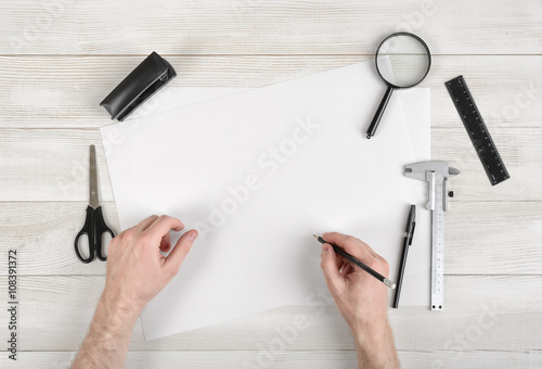 фотографія Closeup hands of man holding pencil and drawing on white paper in top view