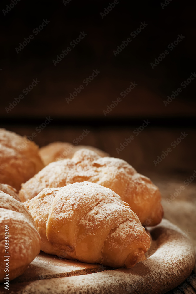 Fresh croissants, sprinkled with powdered sugar, vintage wooden