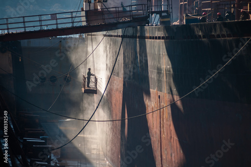 Vászonkép Shipyard worker power washing a ship on dry dock.