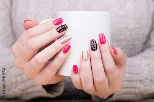 Manicure - Beauty treatment photo of nice manicured woman fingernails holding a cup. Very nice feminine nail art with nice pink, gold and black nail polish.
