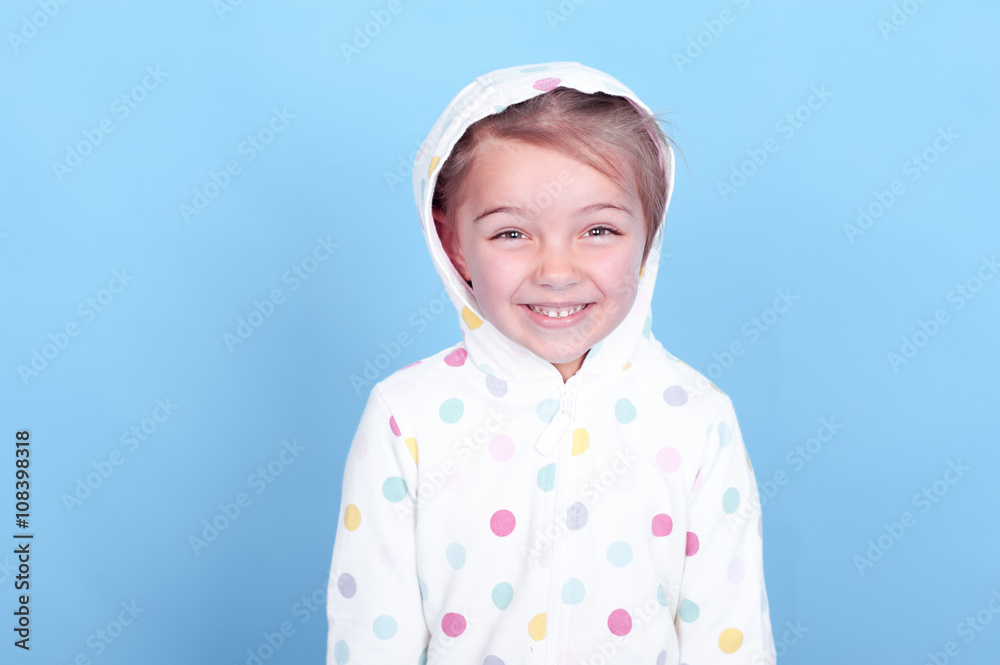 Laughing child girl 3-4 years old posing in room over blue. Wearing hoodie with polka dots. Looking at camera. Having fun. Laughing child girl 3-4 years old posing in room over blue. Wearing hoodie with polka dots. Looking at camera. Having fun.