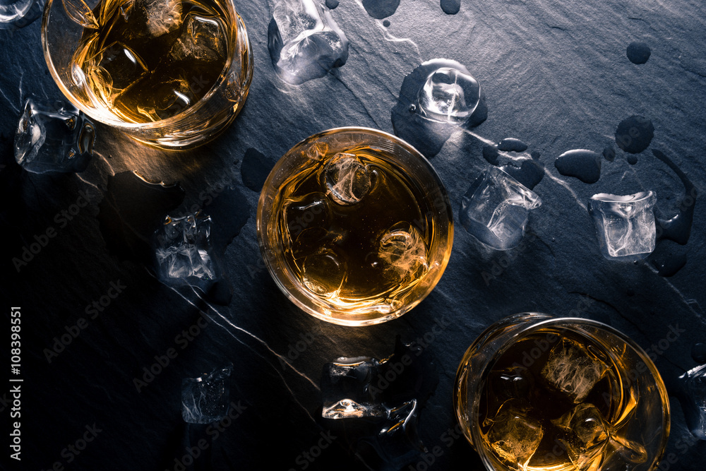 Glasses of whiskey with ice cubes on dark table