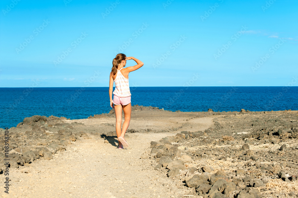 Young beautiful tanned teenage girl walking on Atlantic ocean co
