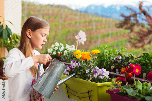 Adorable little girl watering flowers on the balcony photo