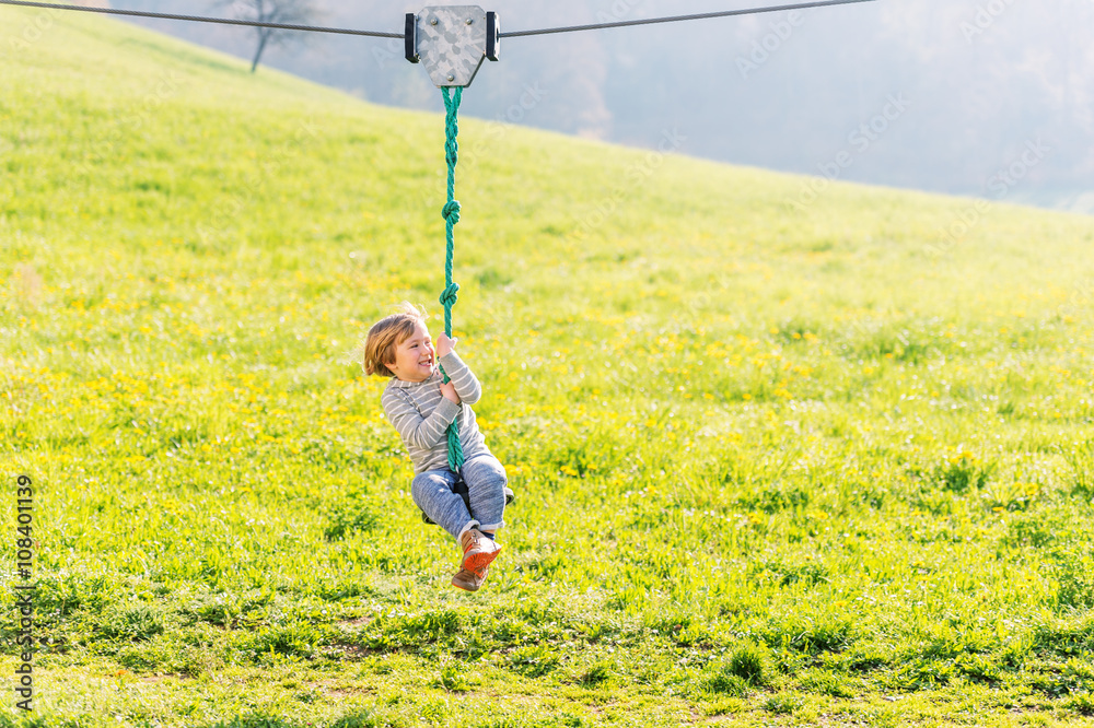 Cute toddler boy playing on a chain swing, having fun in a park on a nice sunny day Cute toddler boy playing on a chain swing, having fun in a park on a nice sunny day