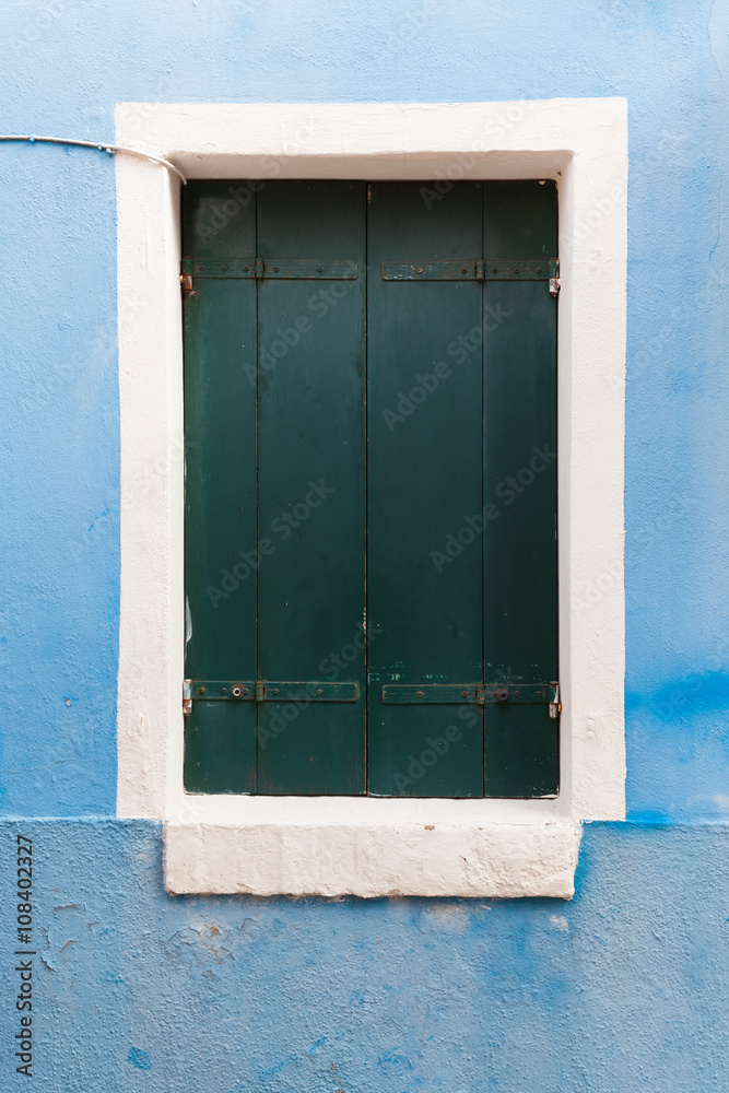 Old window with dark shutters on light blue wall