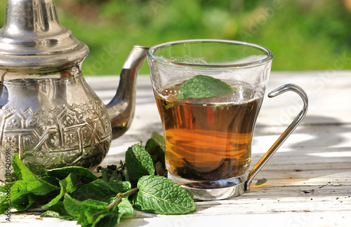 tasse de thé avec feuilles de menthe et théière sur table de jardin  photo