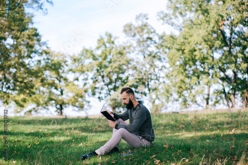 Bearded man hipster student reading a book and relax in park, exams