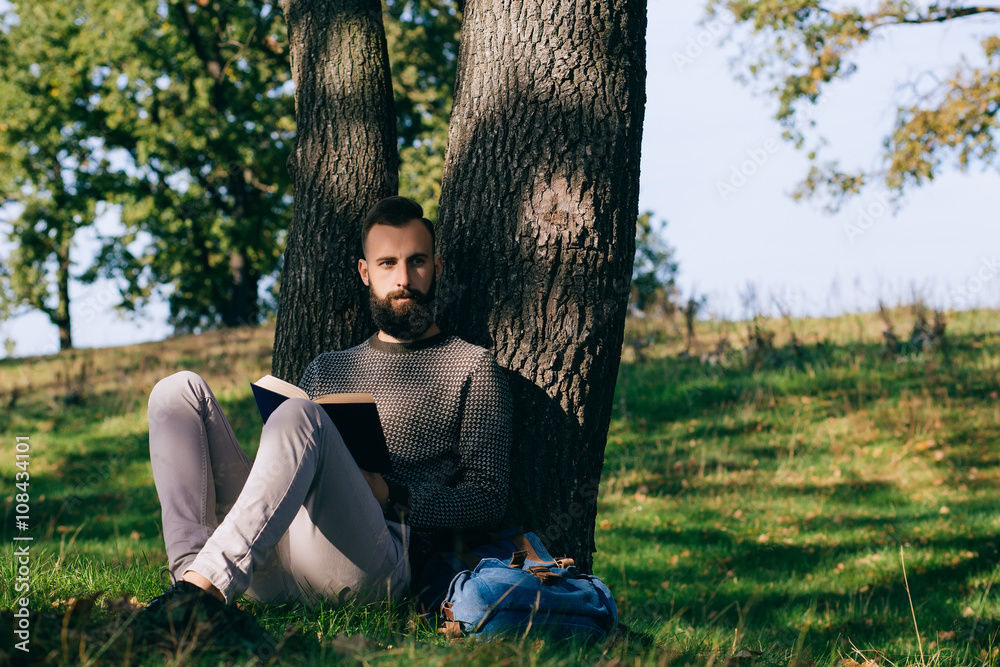 Bearded man hipster student reading a book and relax in park, exams 