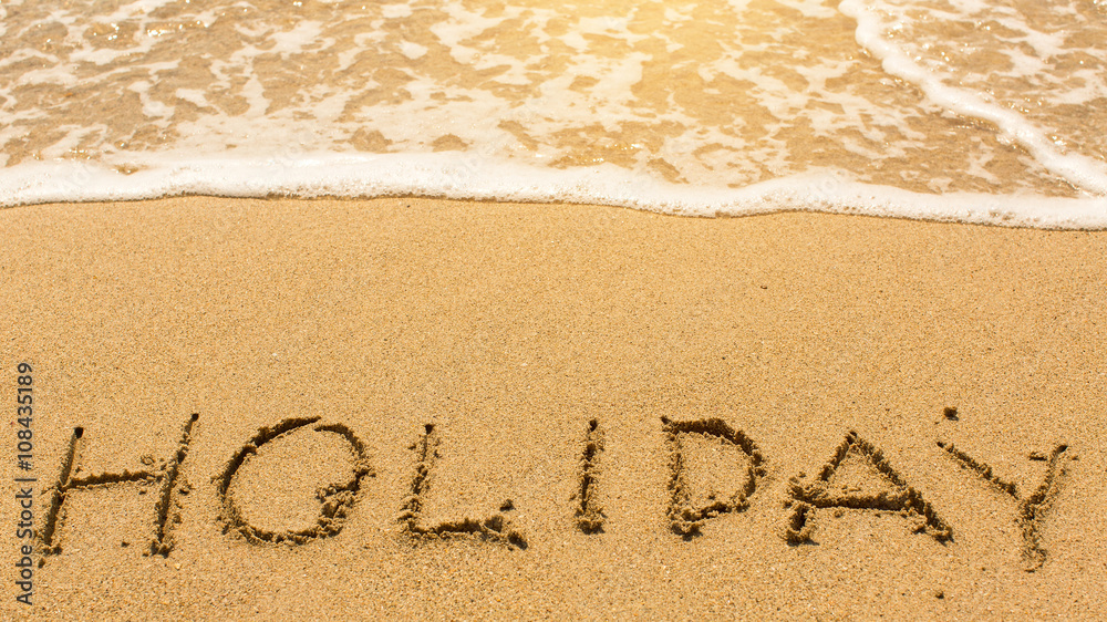 Fototapeta premium Holiday - inscription by hand on yellow beach sand.