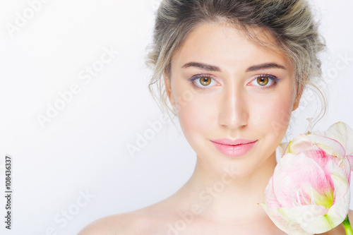 Young beautiful woman with healthy face and nude makeup posing with delicate pink flower on white background