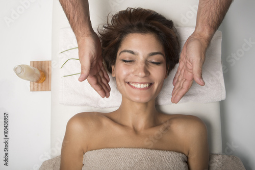 Massaggio al viso a bellissima donna sorridente  distesa su un lettino di un centro benessere. photo