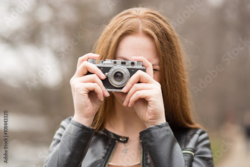 Young woman is taking picture with old fashioned camera, outdoors.