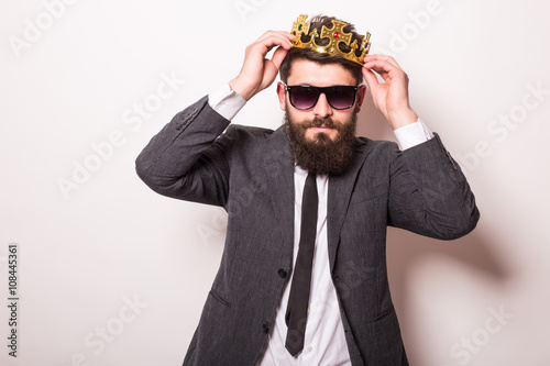 Portrait handsome young cheerful man in suit with crown looking at camera with smile while standing against white background photo