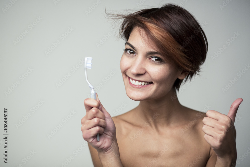 ritratto di ragazza con lo spazzolino in mano che guarda sorridente e che fa il segno di ok - sfondo grigio ritratto di ragazza con lo spazzolino in mano che guarda sorridente e che fa il segno di ok - sfondo grigio