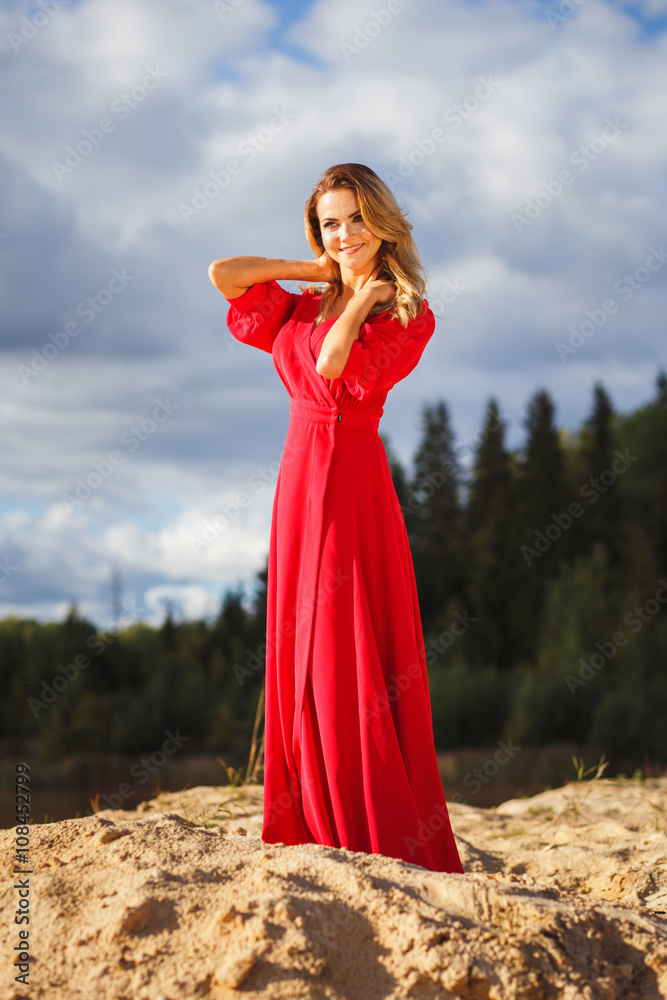 Gorgeous red head young woman in long red dress on a background of a lake. Sandy canyon. Fashion style Gorgeous red head young woman in long red dress on a background of a lake. Sandy canyon. Fashion style