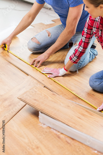 happy couple with ruler measuring parquet board