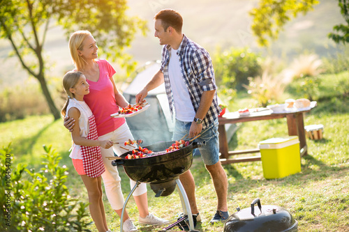 Happy parents grilling meat with daughter.