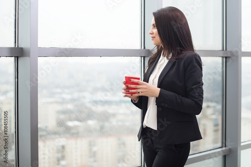Young business woman standing at window with cup of coffee Free Download Young business woman standing at window with cup of coffee - GFXLoad