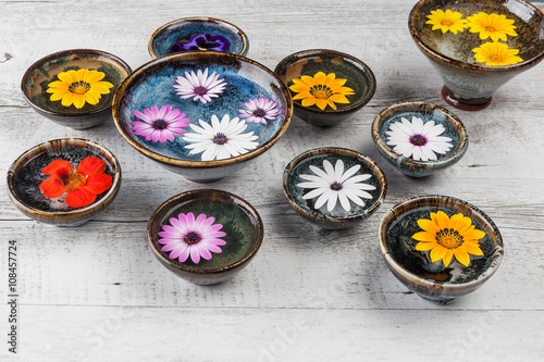Colorful flowers floating in water in ceramic bowls on rustic wooden table.