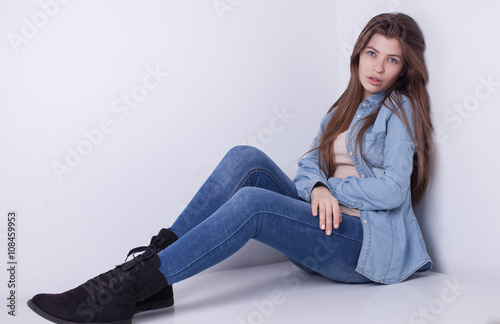 Young European attractive sexy fashion model with long blond natural hair, beautiful eyes, full lips, perfect skin is posing in jeans and shirt in studio for glamour vogue test photo shoot