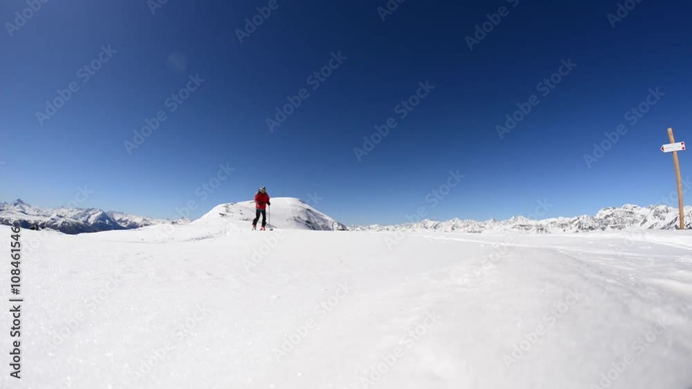 Alpinist ski touring on the ridge with expansive snowcapped mountain view in a bright sunny day. One person hiking towards the camera. Italian French Alps. Alpinist ski touring on the ridge with expansive snowcapped mountain view in a bright sunny day. One person hiking towards the camera. Italian French Alps.