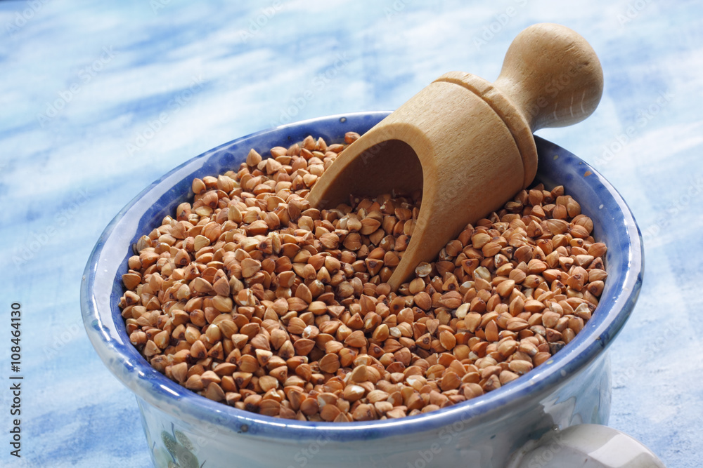 Buckwheat seeds into ceramic cup with wooden scoop Buckwheat seeds into ceramic cup with wooden scoop