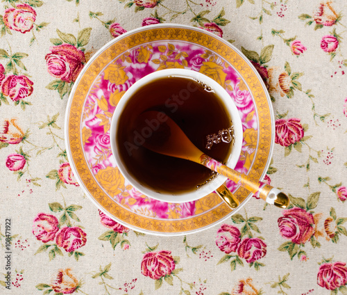 Antique tea cup full of tea on floral background photo