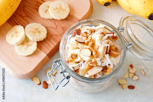 Bananas nut overnight oats with in glass canning jar on white marble, downward view photo