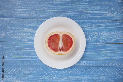 half a grapefruit on white plate on blue wood background