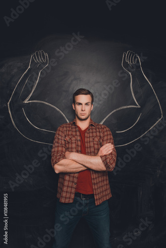 Serious young man with drawn muscular arms on the background of